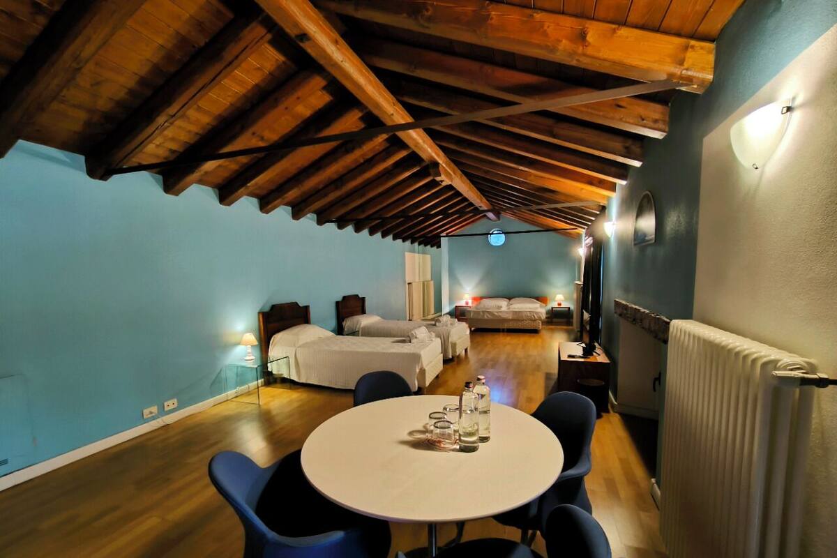A room with a wooden ceiling, a round table with chairs, a bed, and a radiator.