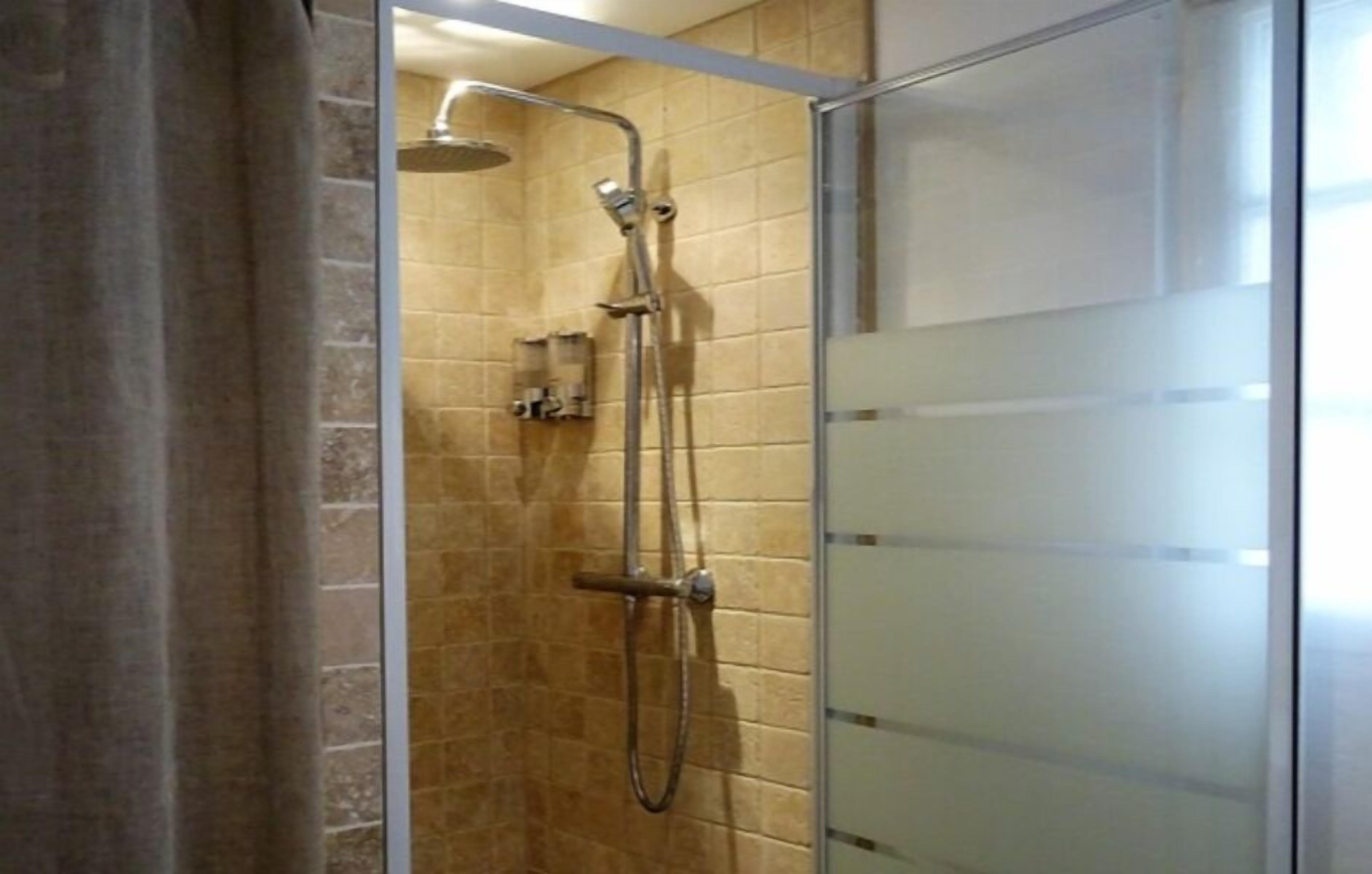 A glass-enclosed shower with a handheld showerhead and a wall-mounted faucet.