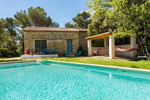 Un edificio de piedra con piscina, mobiliario exterior y una hamaca.