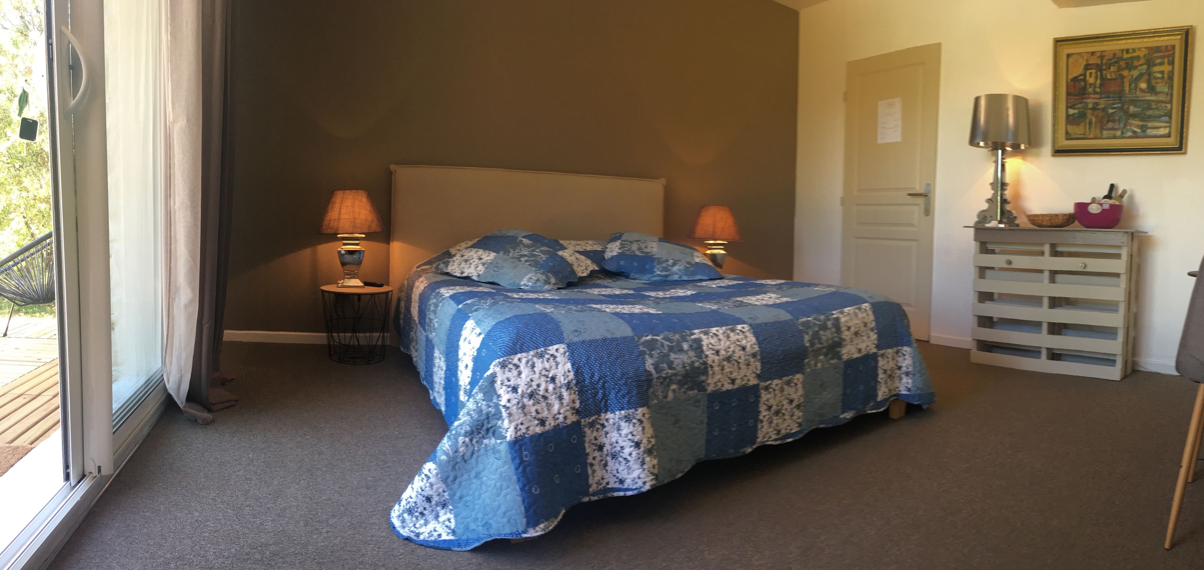 A bedroom with a large bed, two bedside lamps, a dresser with drawers, and a painting on the wall.