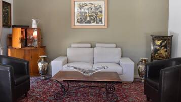 A living room with a white sofa, two black armchairs, a coffee table, a red patterned rug, and a framed abstract painting on the wall.