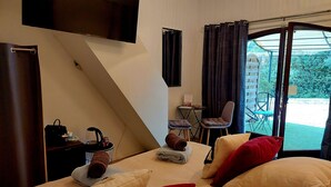 Un dormitorio con cama, almohadas, una mesita con silla, televisor y vista al exterior.