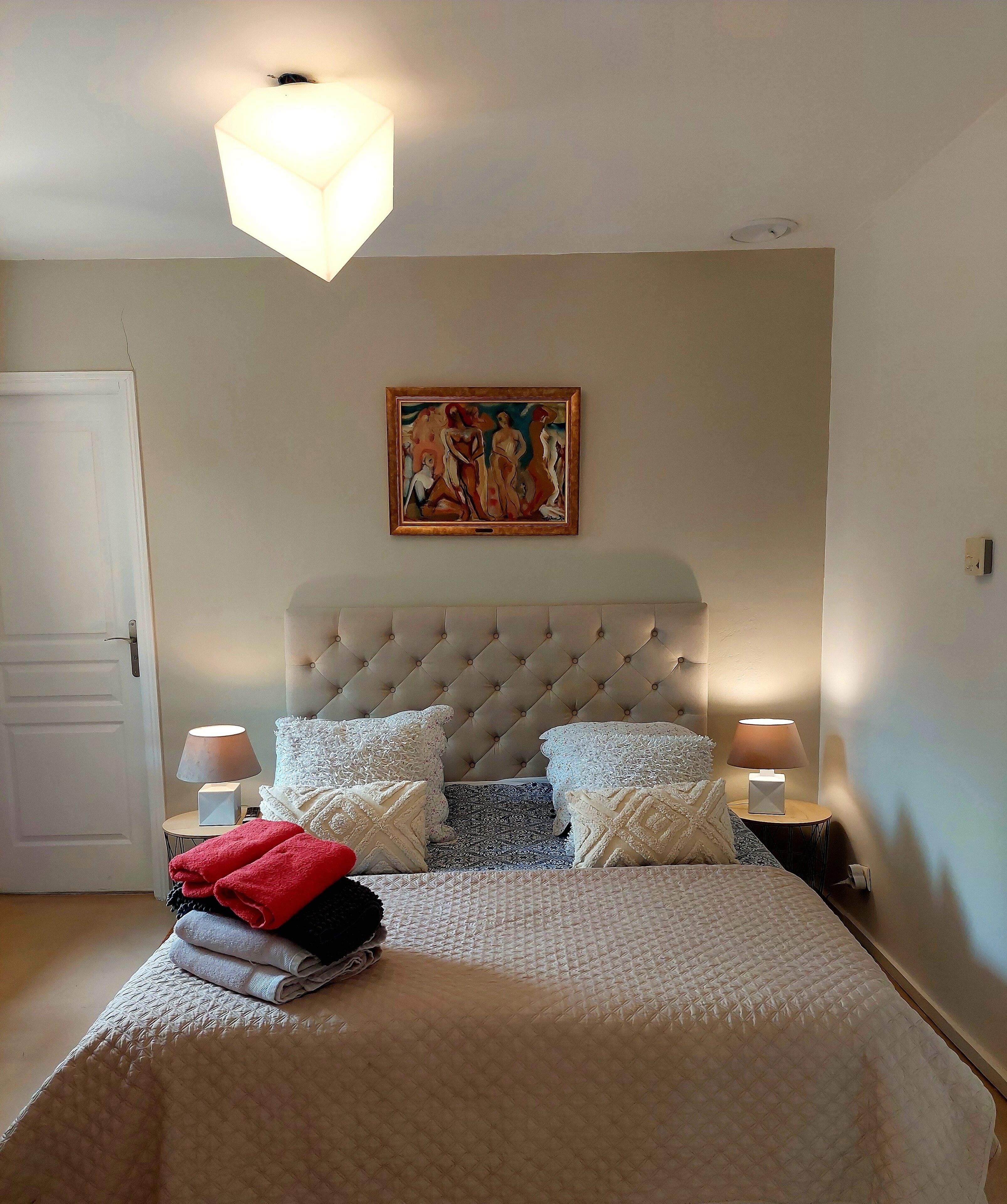 Une chambre à coucher avec une tête de lit capitonnée, un tableau au-dessus du lit et deux lampes de chevet.