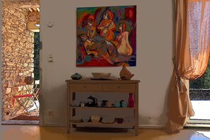 Una habitación con un cuadro en la pared, una consola de madera con vajilla y vistas por una ventana.