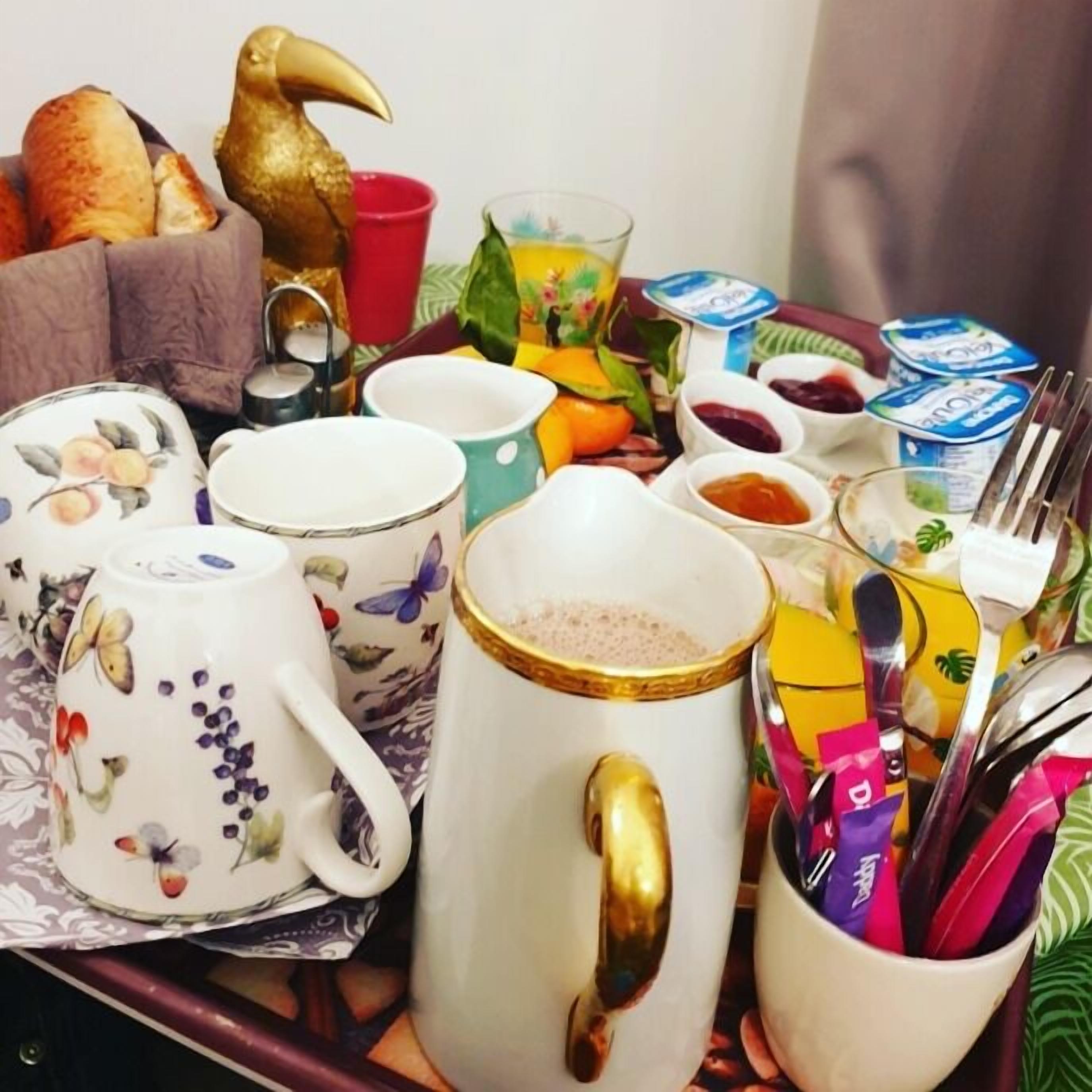 Ein Frühstücksbrett mit verschiedenen Gegenständen, darunter ein Teekessel, Tassen, eine Karaffe und Besteck.
