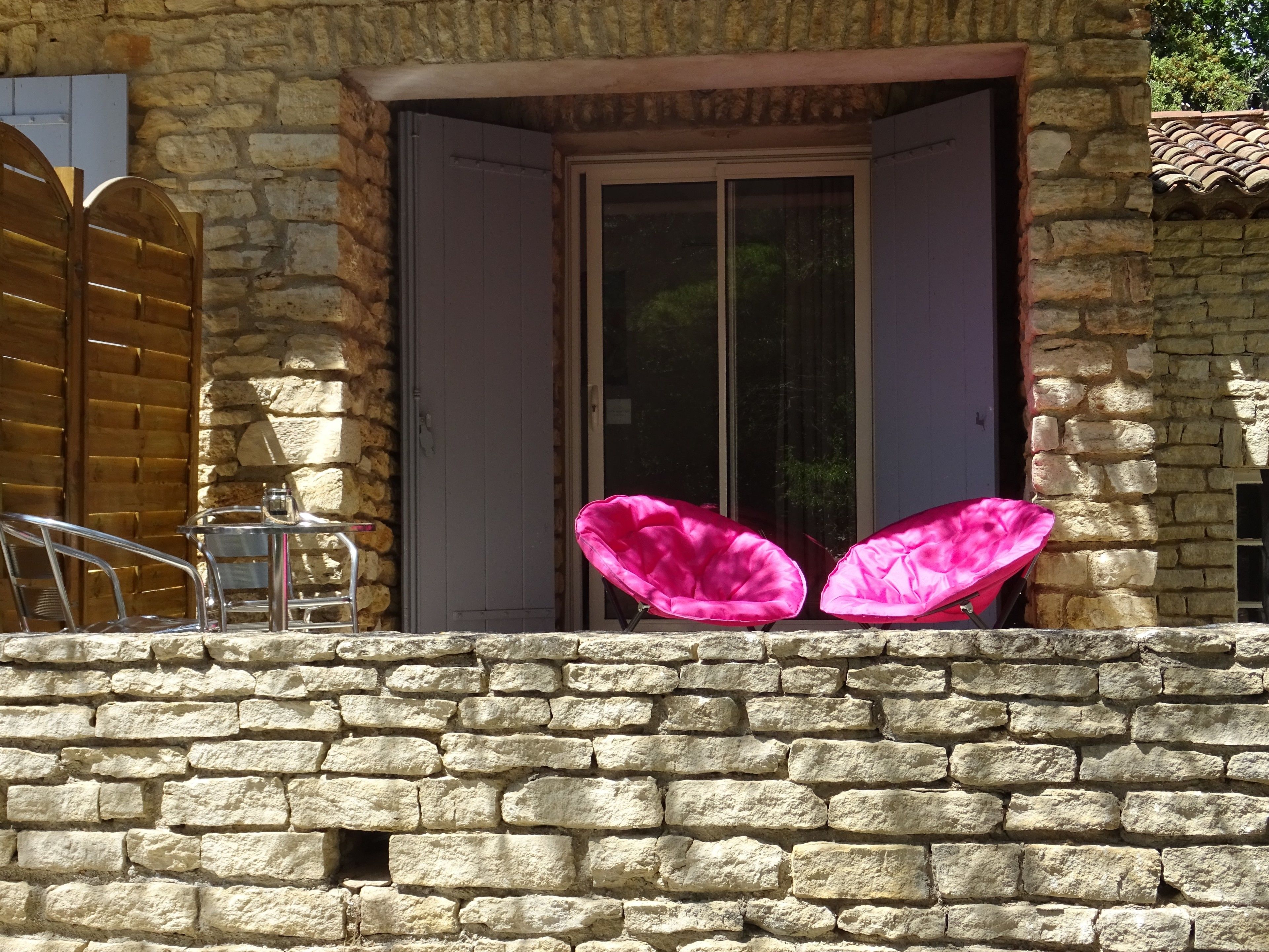 A stone building with a wooden door and a window. There are two pink chairs outside the door.