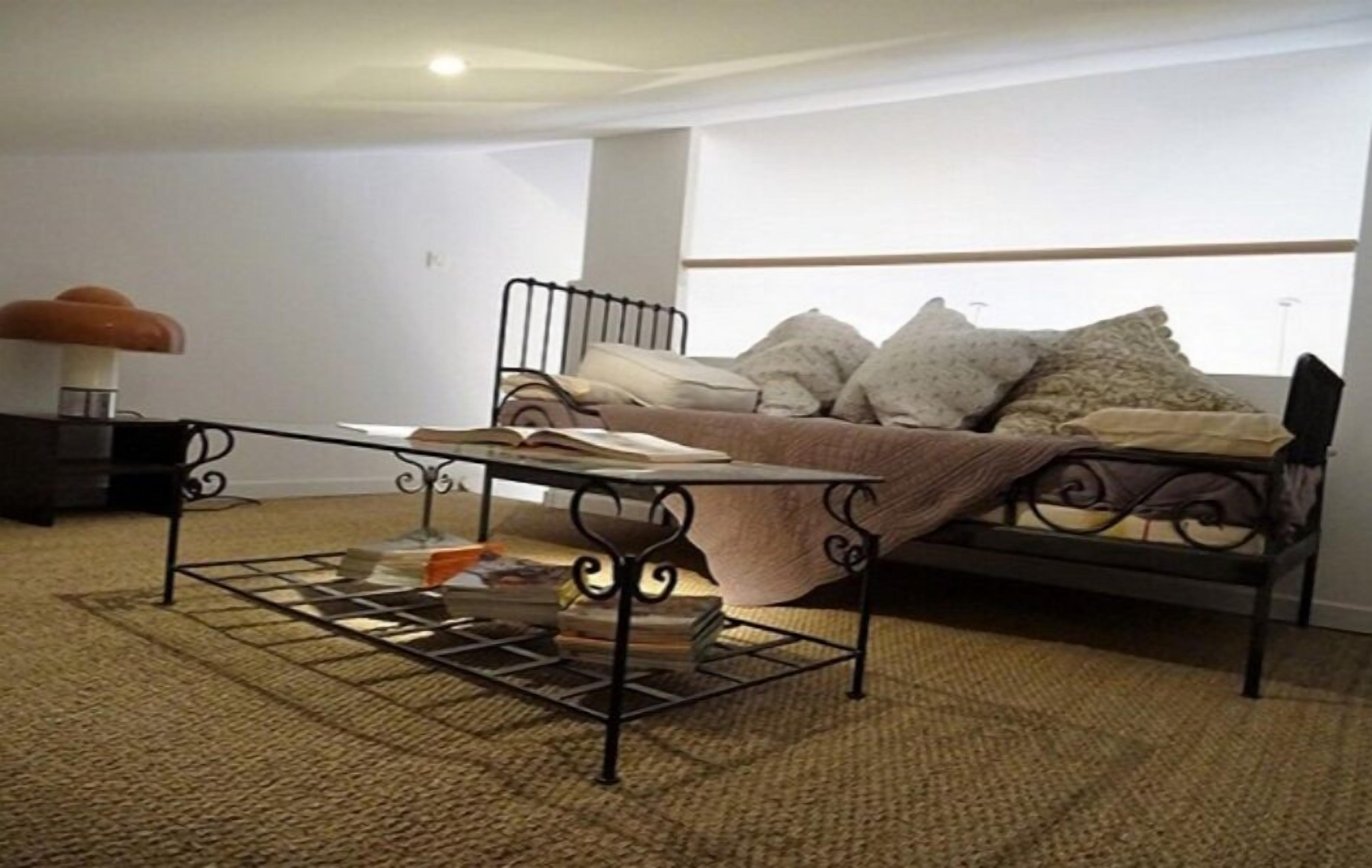 A bedroom with a metal bed frame, a bedside table, a lamp, and a window with a view.