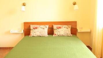 A room with a green bedspread, two floral pillows, a wooden headboard, and two bedside tables with lamps.