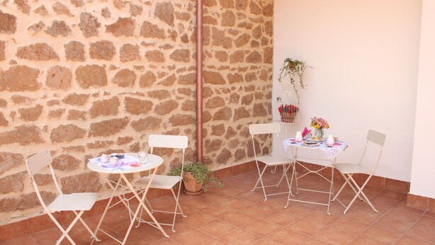 A stone-walled patio with four white folding chairs and a small table, a potted plant, and a hanging plant.