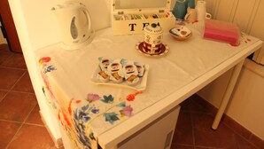 A table with a floral tablecloth, a white kettle, a tea box, and a pink container.