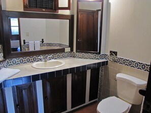Un baño con lavamanos blanco, armarios de madera oscura, inodoro blanco y espejo sobre el lavamanos.