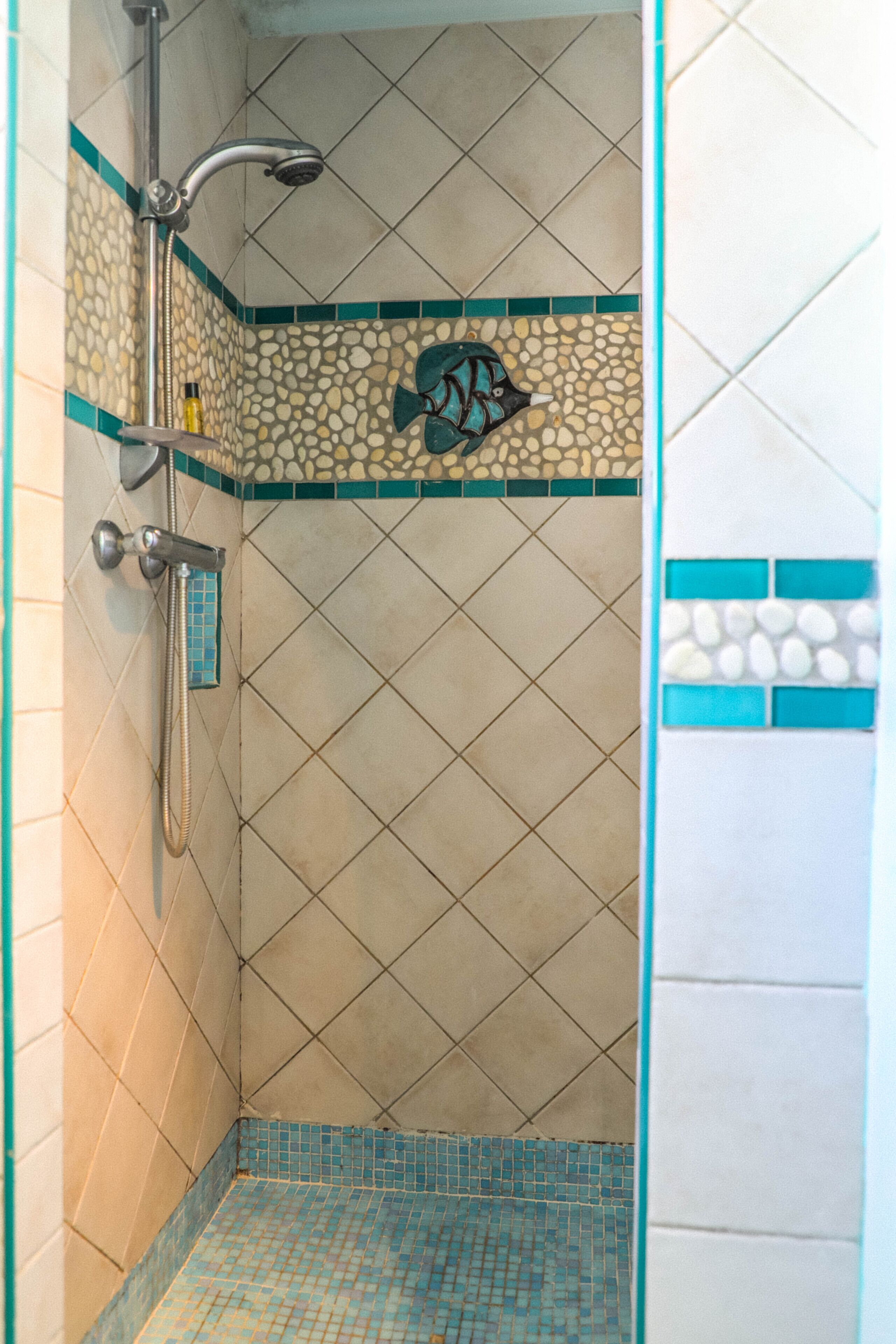 A bathroom with a shower, tiled walls, and a decorative fish mosaic.