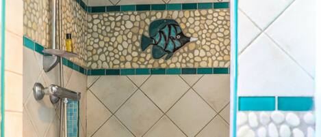 A bathroom with a shower, tiled walls, and a decorative fish mosaic.