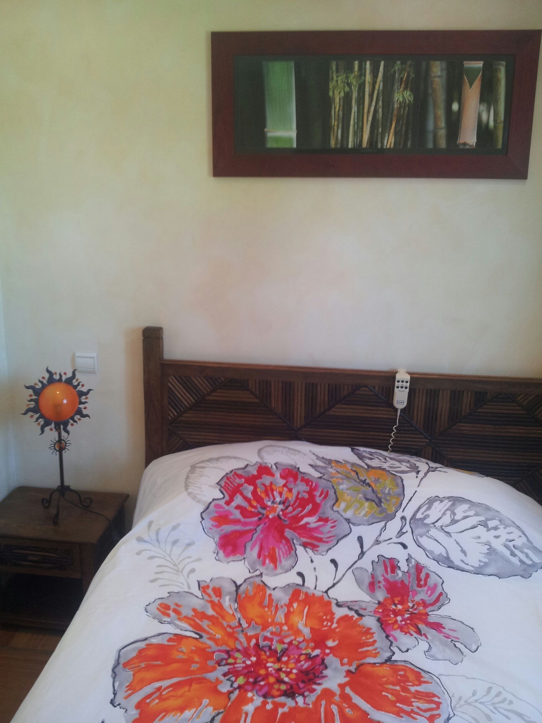 Une chambre à coucher avec un lit agrémenté d’une couvre-lit à motifs floraux, d’une tête de lit en bois, d’une table de chevet avec une lampe et d’un tableau encadré au mur.