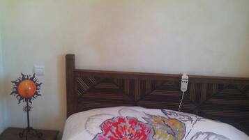 Un dormitorio con una cama con colcha estampada, cabecera de madera, mesita de noche con lámpara y un cuadro en la pared.