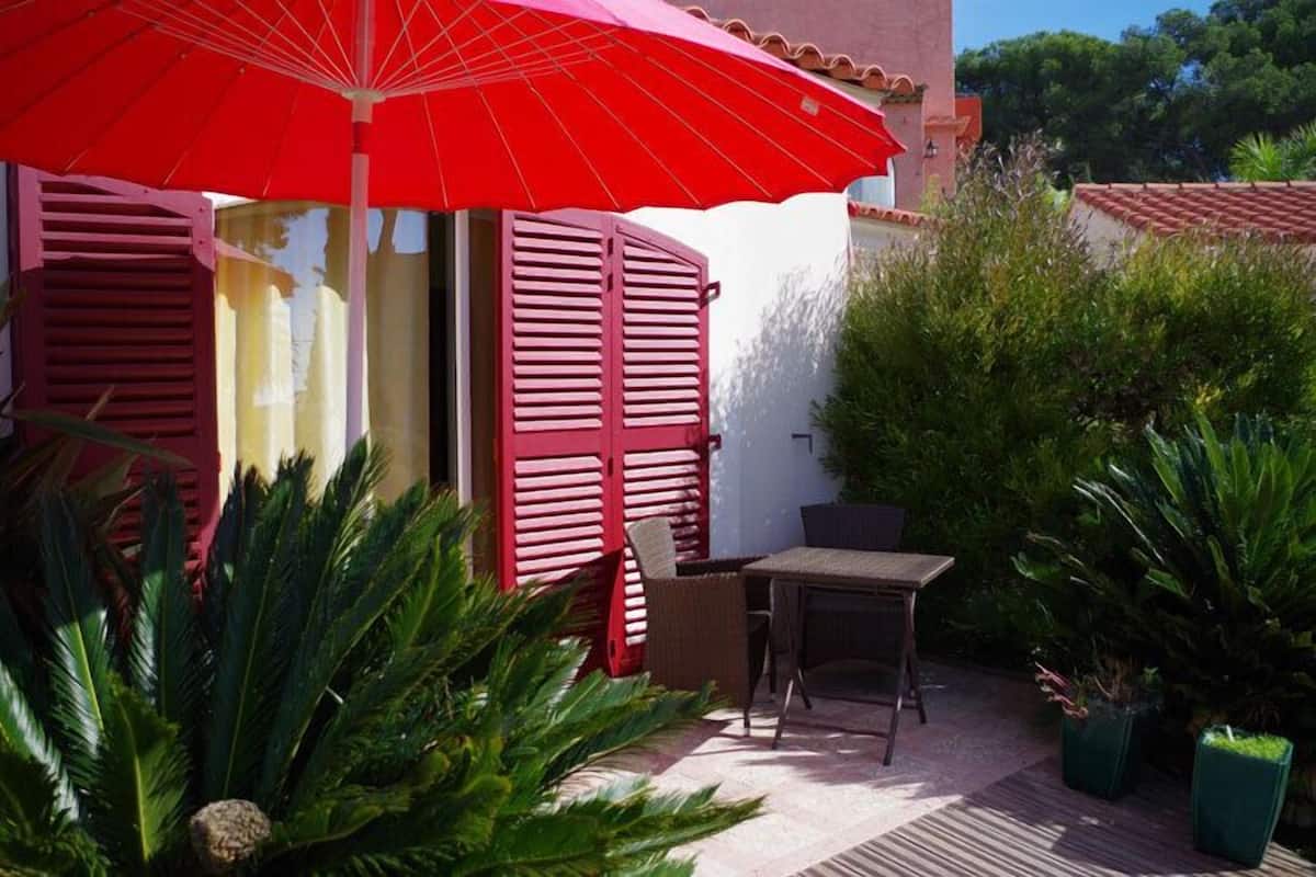 Eine Terrasse mit rotem Sonnenschirm, einem Tisch und Stühlen.