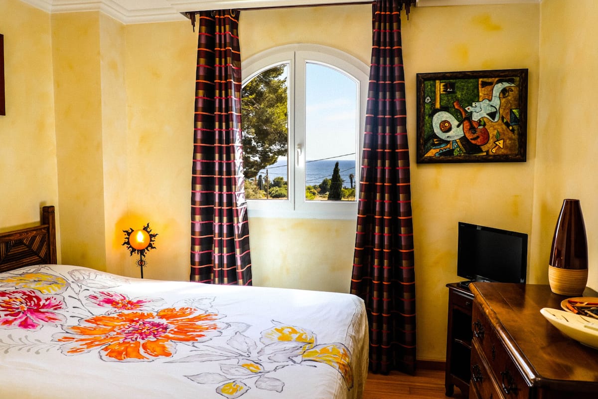 Ein Hotelzimmer mit Bett, Schreibtisch, Fernseher, Lampe und einem Fenster mit Vorhängen.