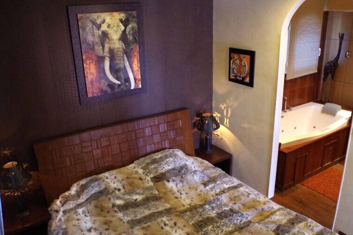 Ein Schlafzimmer mit einem Bett, einem Nachttisch, einem Elefantenbild und einem Badezimmer mit einer Badewanne sowie einer Giraffendekoration.