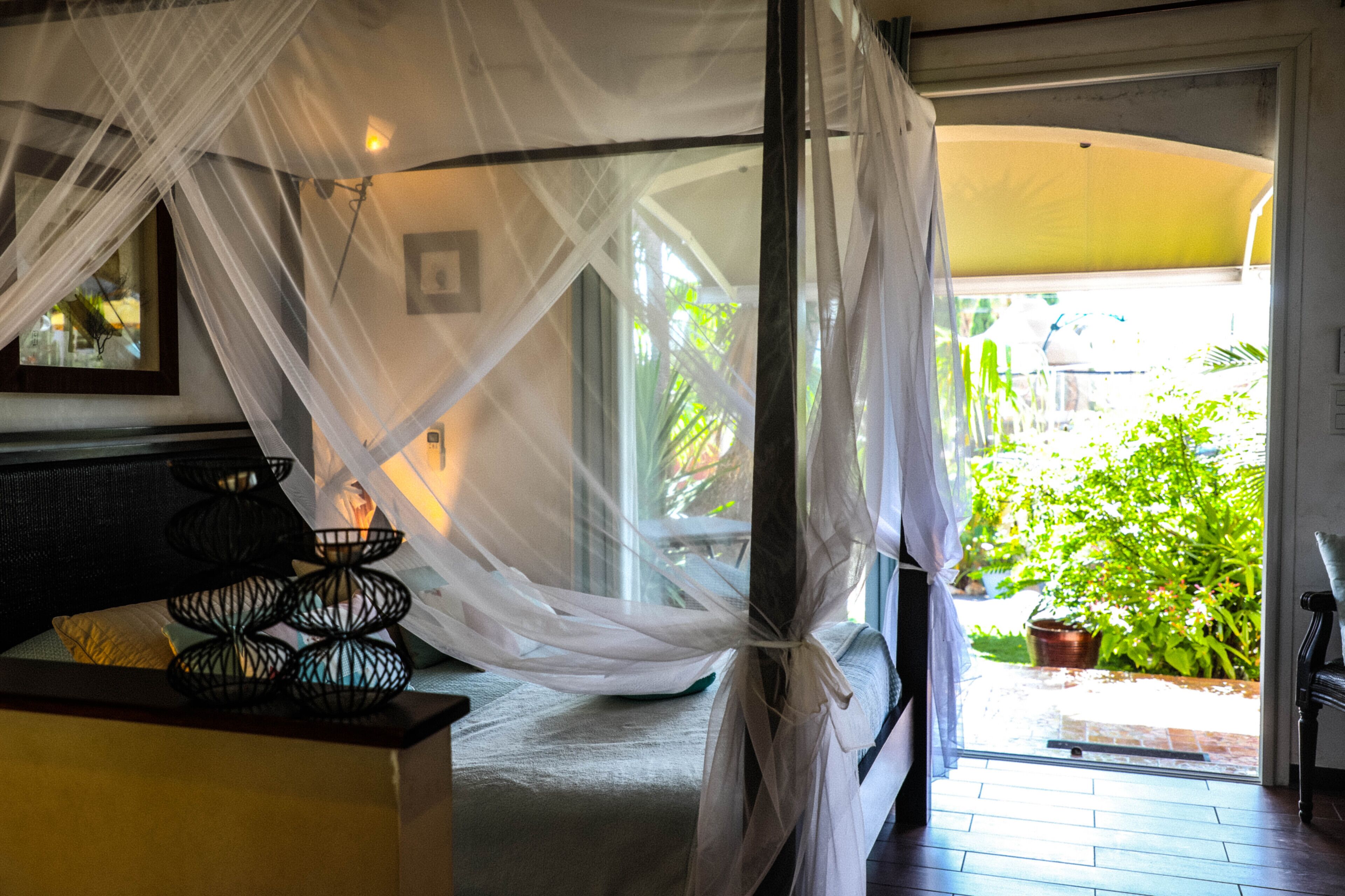 Une chambre avec un lit recouvert d’une moustiquaire, une fenêtre donnant sur un paysage verdoyant et une porte menant à l’extérieur.