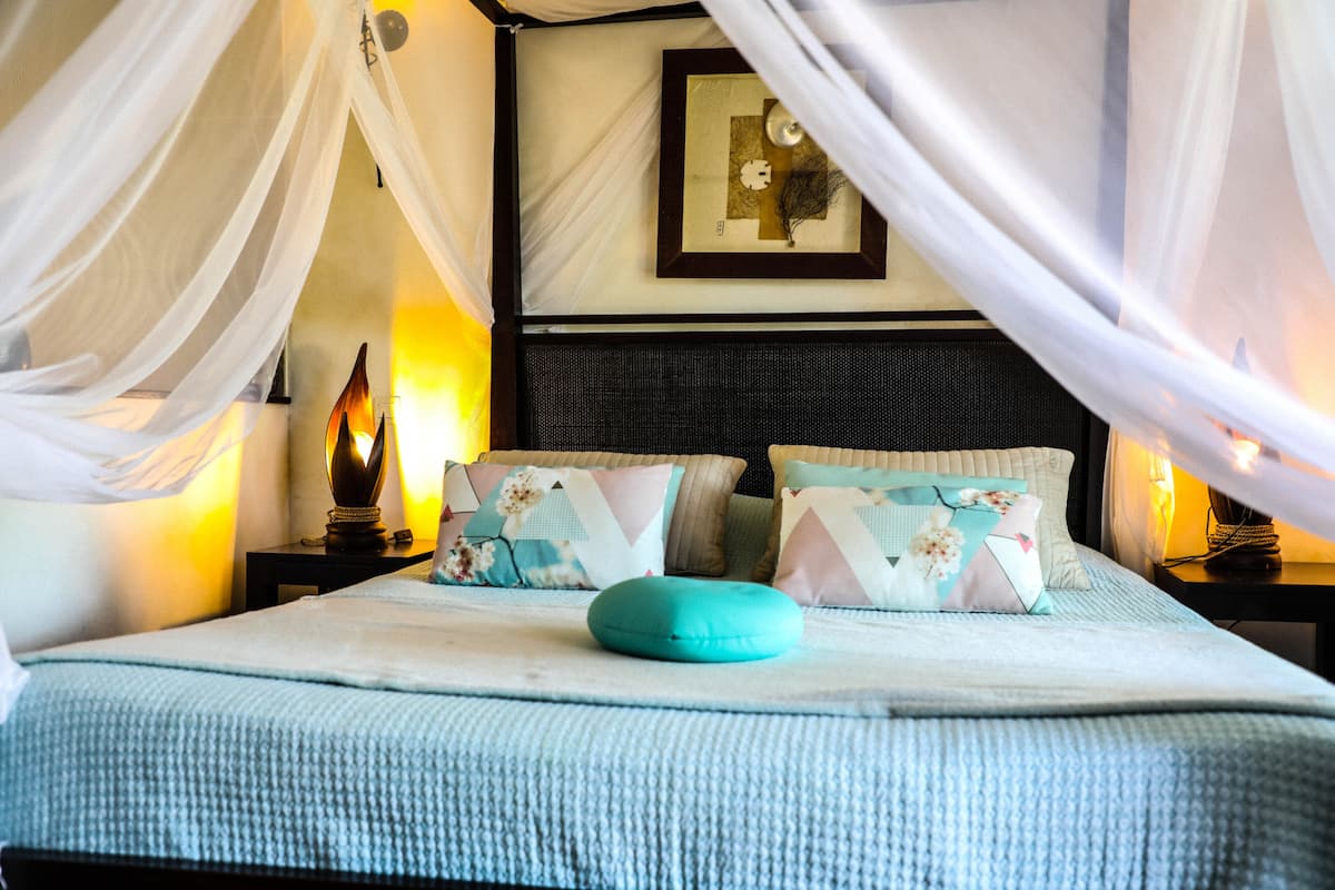 Ein ordentlich bezogenes Bett mit blauer Decke, weißen Kissen und einem Kissen in Türkis.