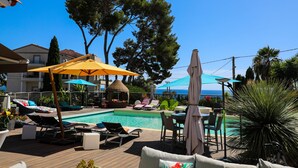A poolside area with lounge chairs, umbrellas, and a small table. - Val D'azur Chambres D'hôtes de Charme (Carqueiranne)