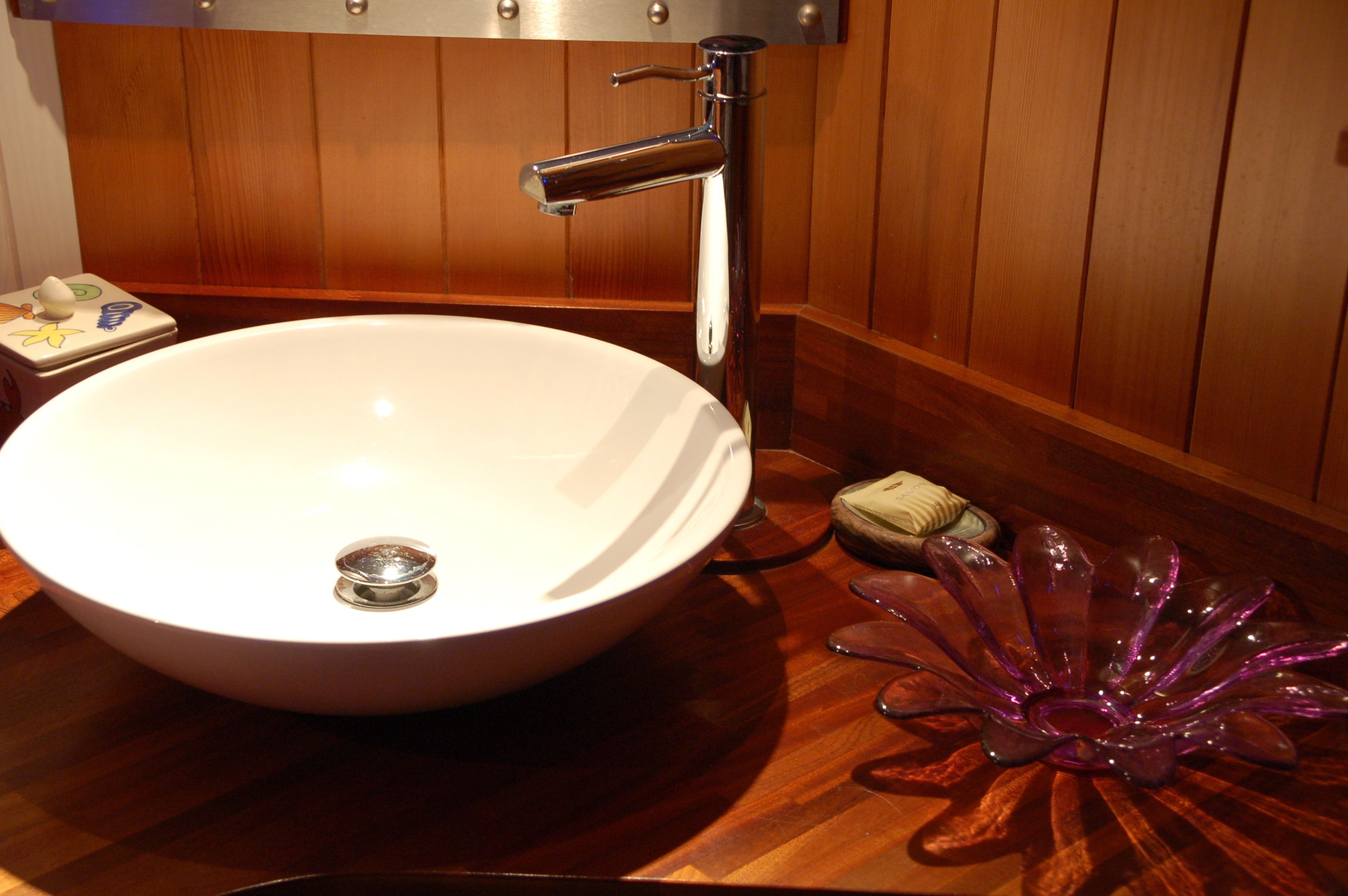 A white sink with a chrome faucet, a soap dish, and a decorative glass piece on a wooden countertop.