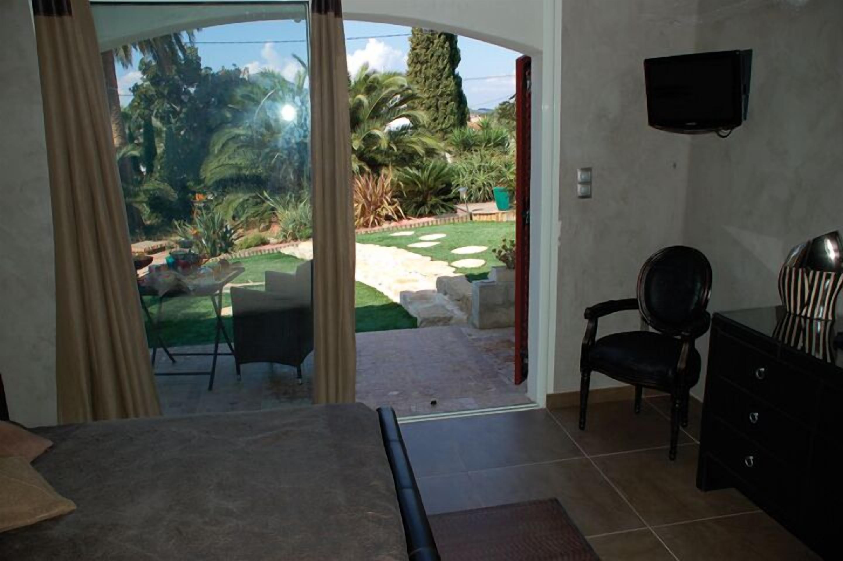 Une pièce dotée d’une porte-fenêtre coulissante donnant sur un jardin. On y trouve une chaise, une petite table et un téléviseur fixé au mur.