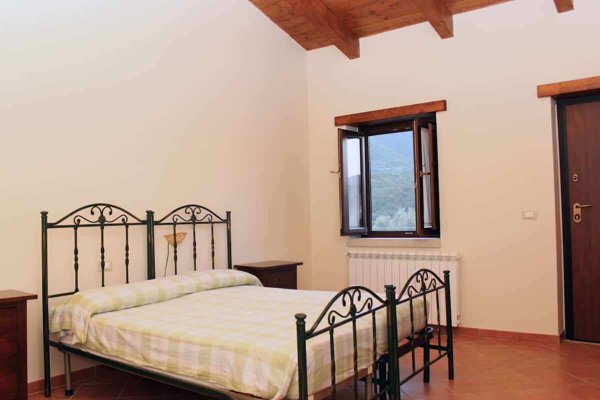 Une chambre à coucher avec un lit en métal, une fenêtre donnant sur un paysage agréable, un radiateur et une porte en bois.