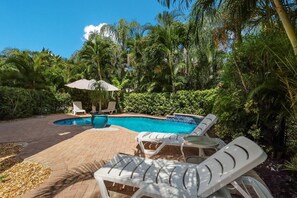 Une piscine entourée d’une végétation luxuriante, avec des chaises longues et des parasols.
