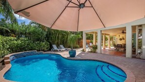 A swimming pool with lounge chairs and an umbrella, surrounded by greenery. - Sunkissed 3 Bedroom Townhouse by RedAwning (Holmes Beach)