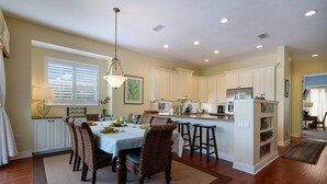 A spacious kitchen with white cabinets, a dining area with wicker chairs, and a central island with stools. - Sunkissed 3 Bedroom Townhouse by RedAwning (Holmes Beach)
