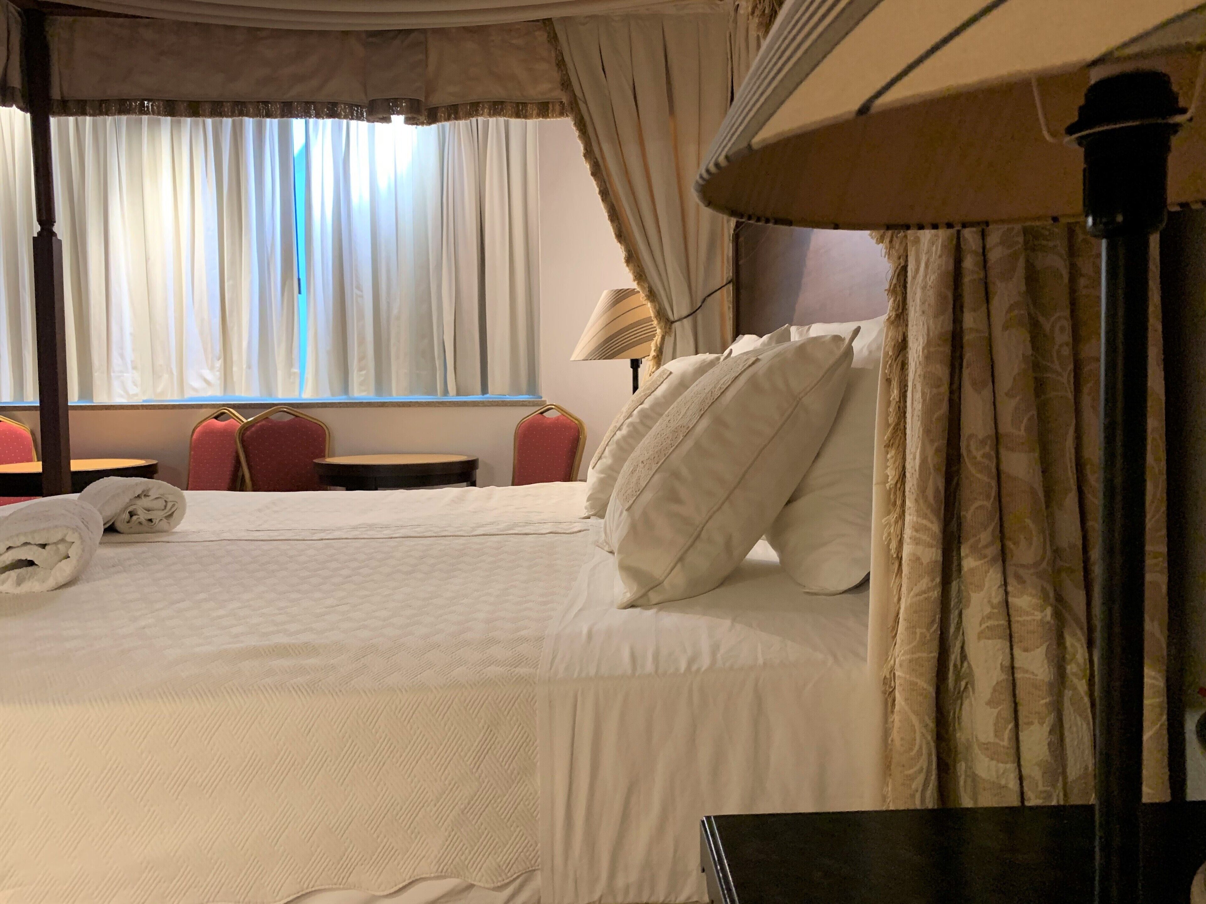A hotel room with a bed, two red chairs, a round table, and a lamp.