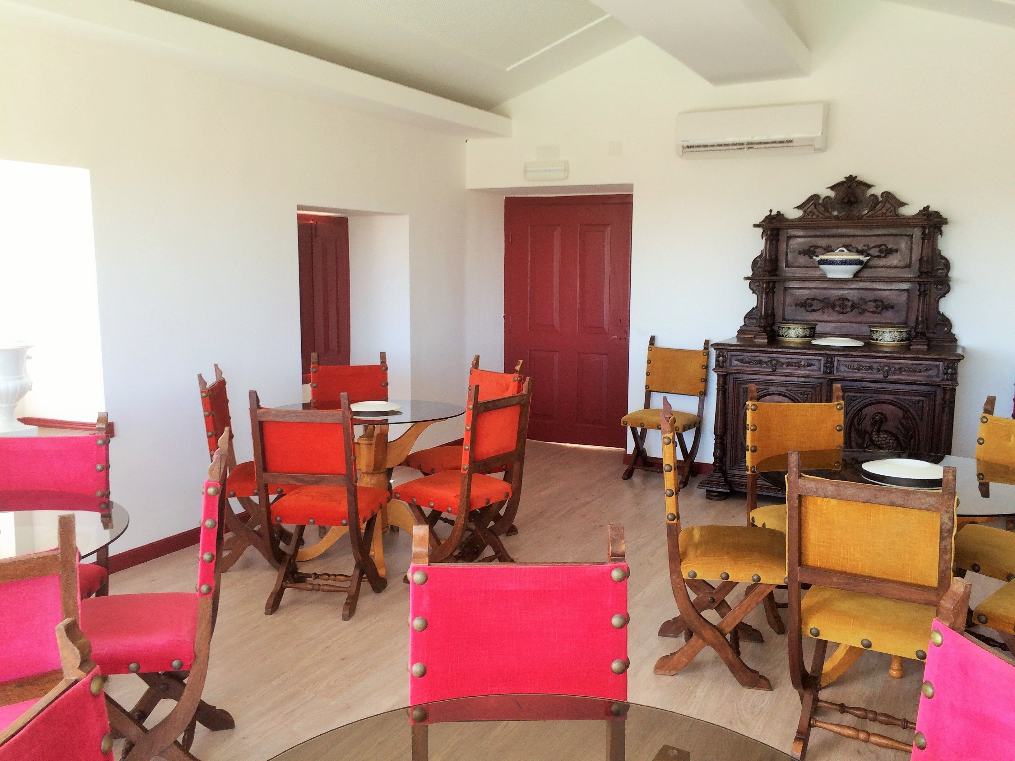 Un comedor con una mesa redonda y varias sillas, una puerta roja y un armario de madera con adornos.