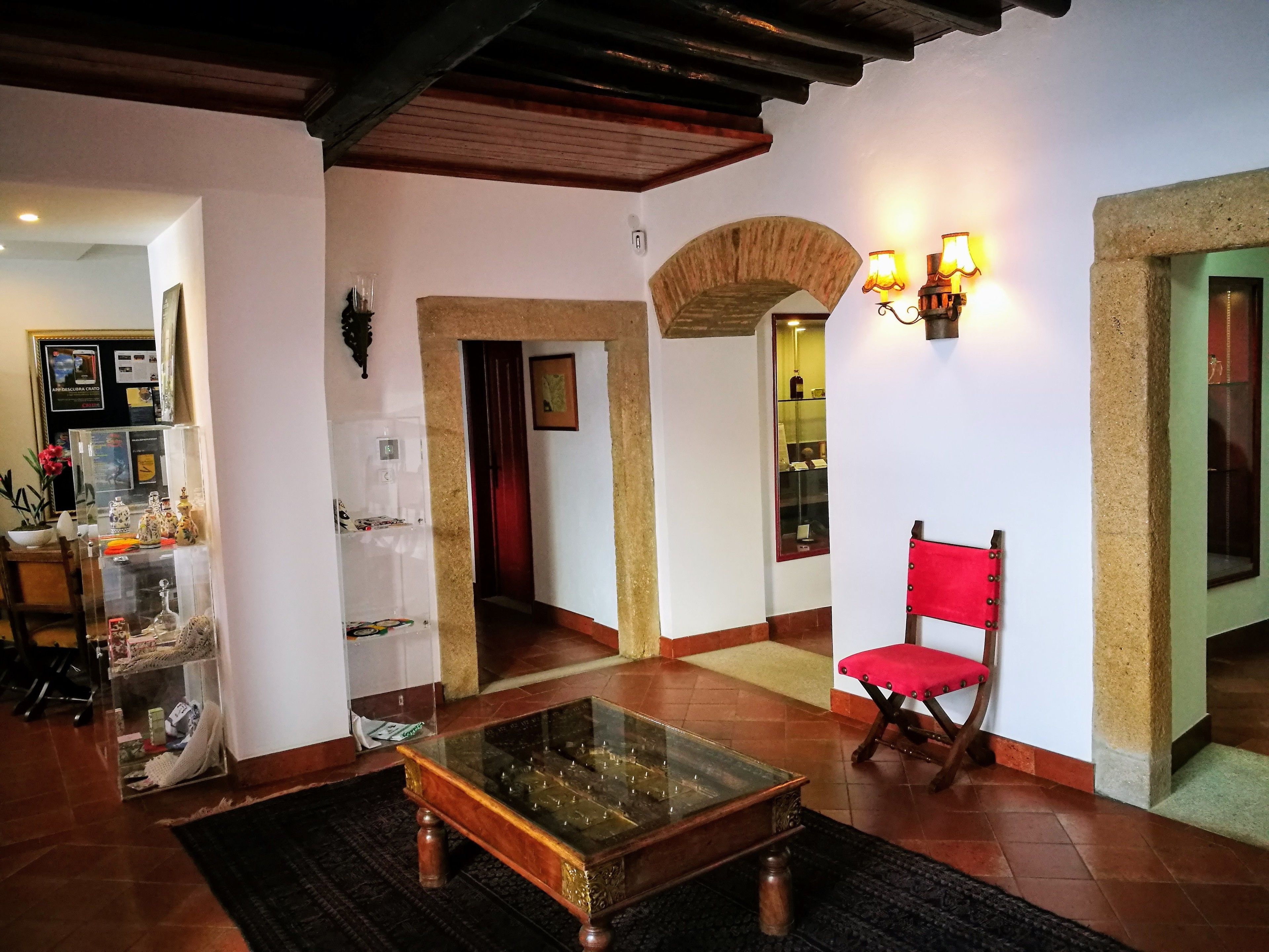 Uma sala de estar ampla com uma mesa de centro de vidro, uma cadeira vermelha e um arco de pedra.