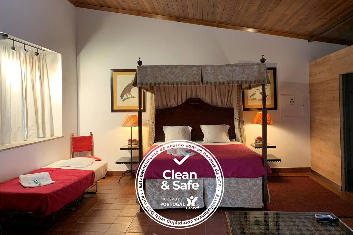 A hotel room with a four-poster bed, two single beds, a wooden ceiling, and a red carpet.