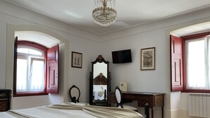 Un dormitorio con una cama grande, un aparador, un espejo, un televisor y una ventana con contraventanas rojas.