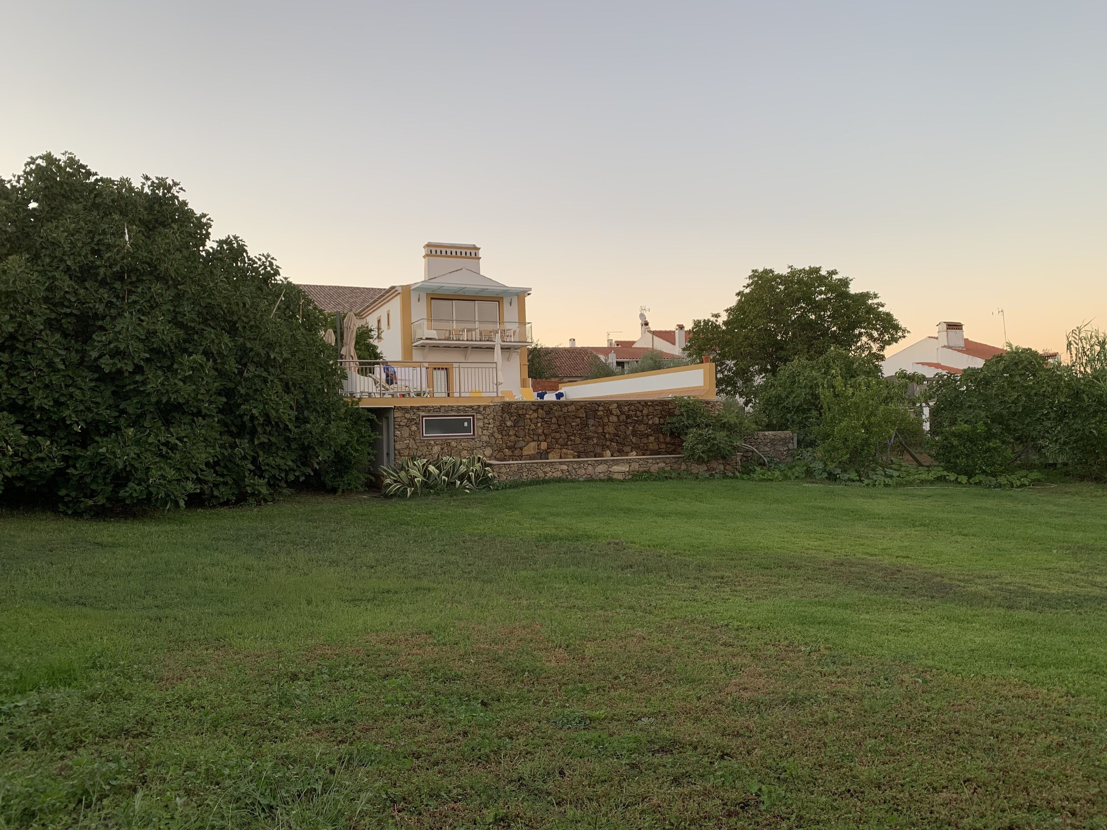 Una casa con un muro de piedra, un balcón y un patio con césped.