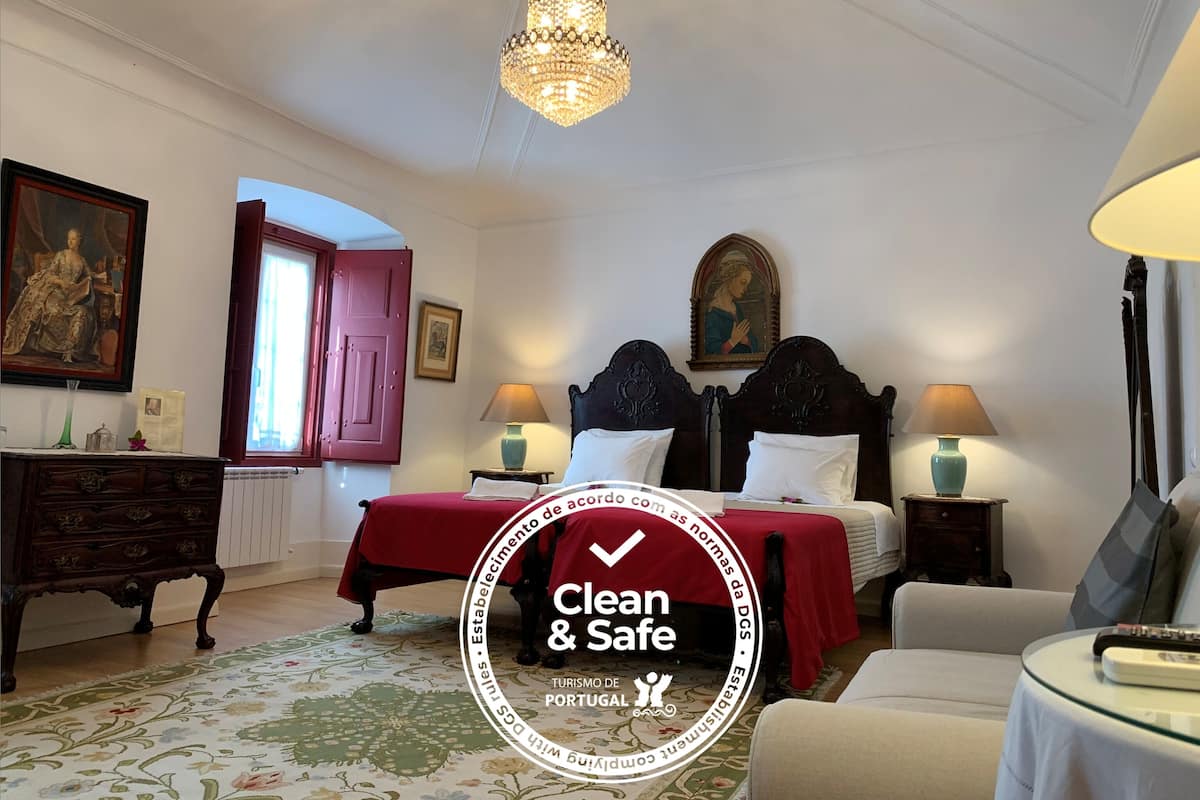 A hotel room with a bed, two bedside tables with lamps, a dresser, a chandelier, and a painting on the wall.