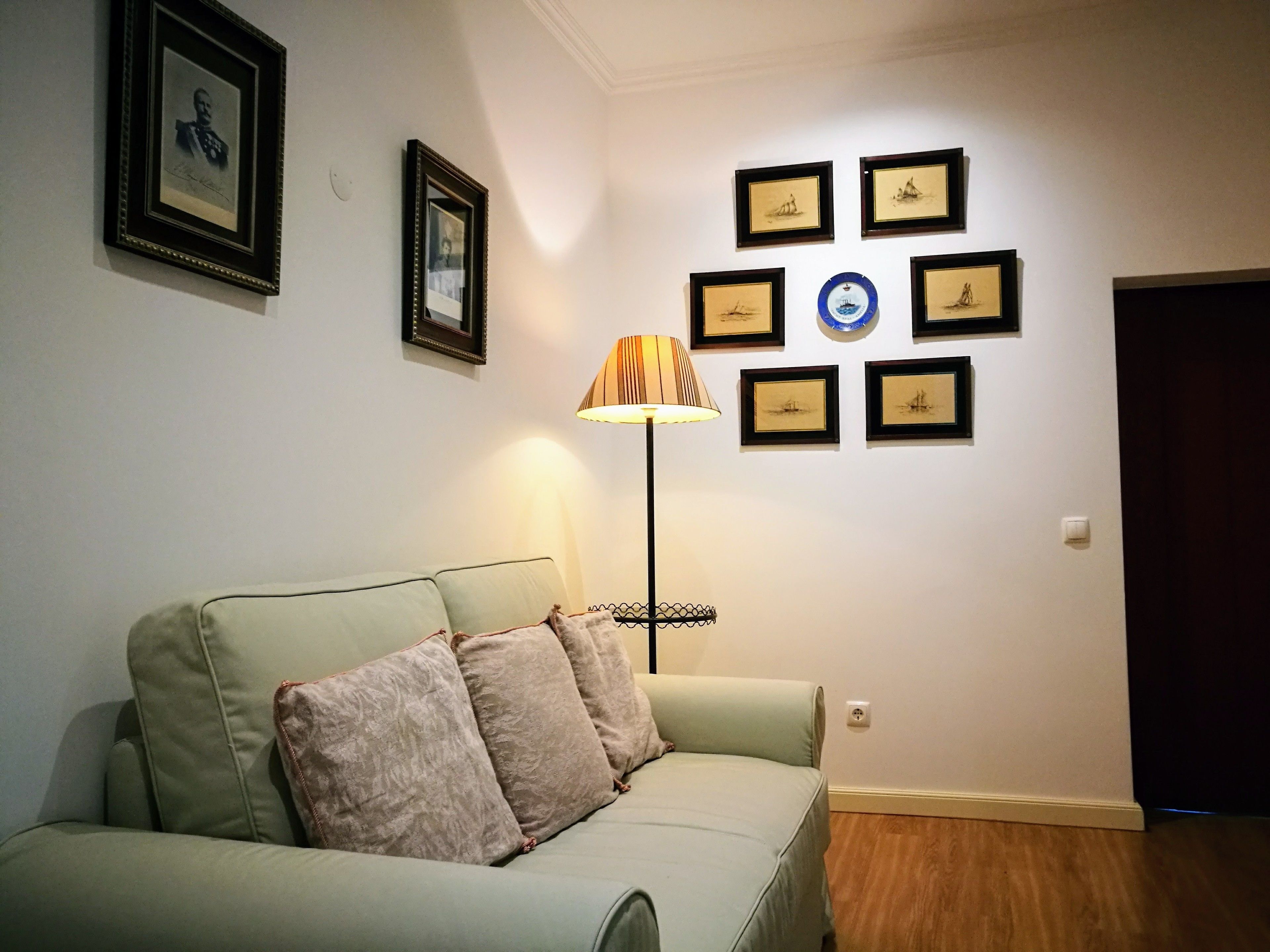 A living room with a sofa, a lamp, and several framed pictures on the wall.
