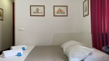 A hotel room with a bed, two framed pictures on the wall, a red curtain, and a white headboard.