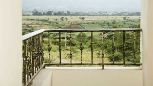 Un balcón con barandilla de hierro forjado que da a un paisaje verde con árboles y colinas lejanas.