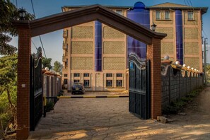 Une entrée fermée par un portail, surmontée d’une arche en briques, mène à un bâtiment doté de grandes structures cylindriques.
