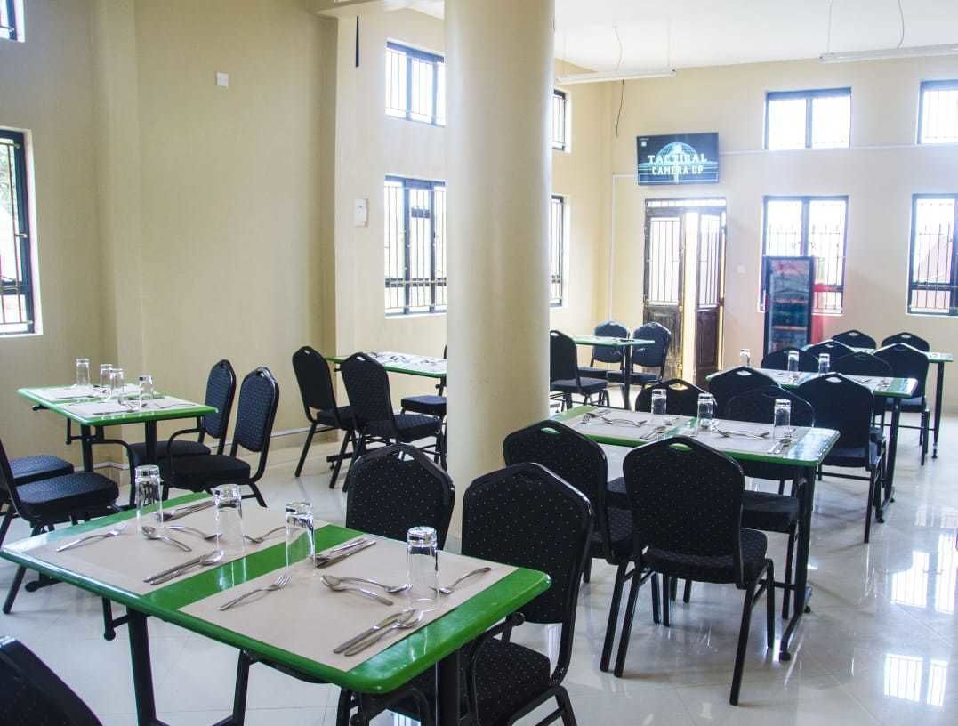 A dining area with tables set for four, each with cutlery and glasses. There are multiple windows allowing natural light.