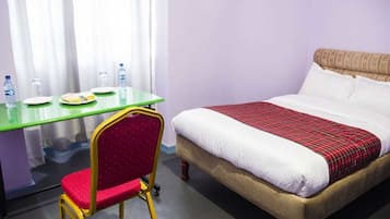 A hotel room with a bed, a green table with plates and water bottles, and a red chair.