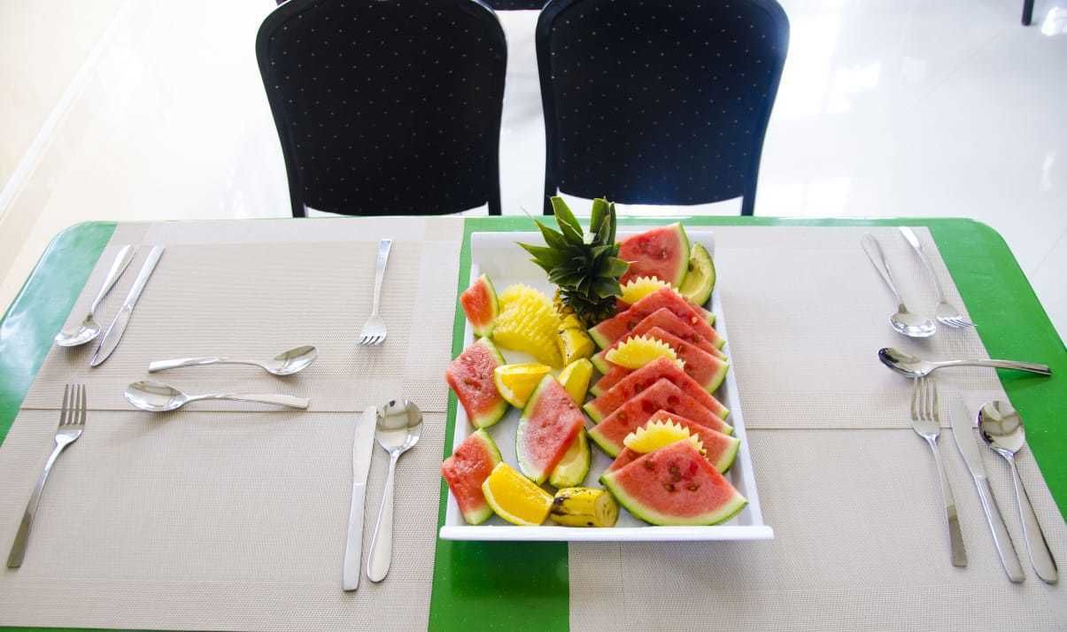 A dining table set with a fruit platter, cutlery, and two chairs.
