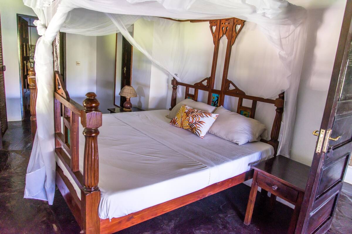 A bed with a canopy, wooden headboard, and a bedside table with a lamp.