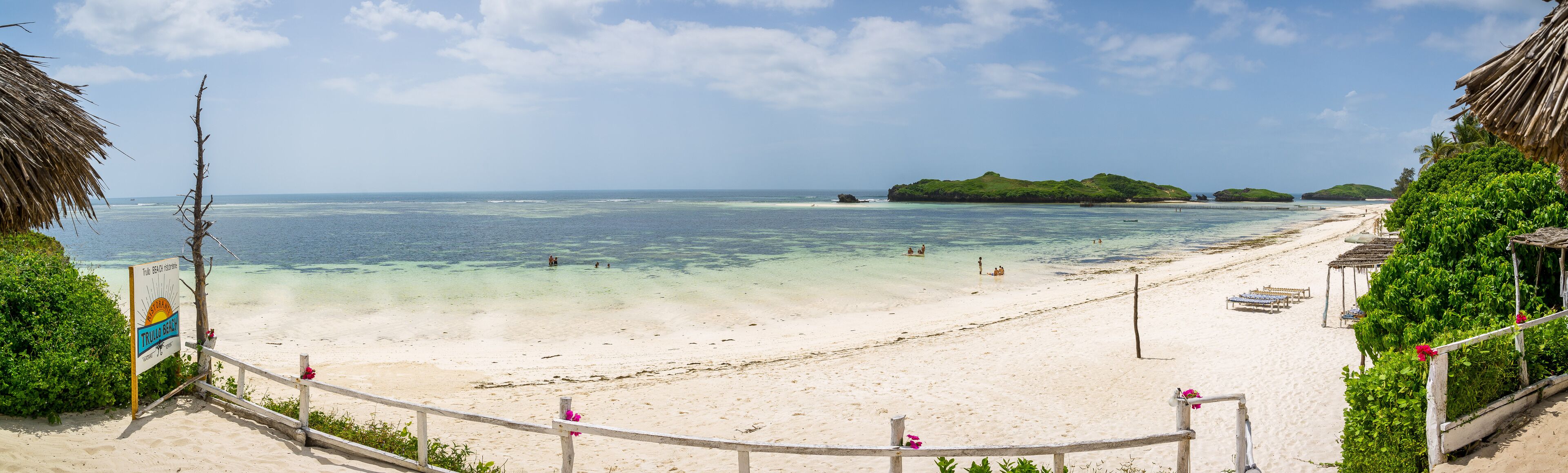 A beach with clear turquoise water, a sandy shore, and a sign indicating 'Trullo Beach'.