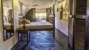 A room with a bed, a table, a mirror, and a window with shutters. - Ocean Breeze Villa (Watamu)