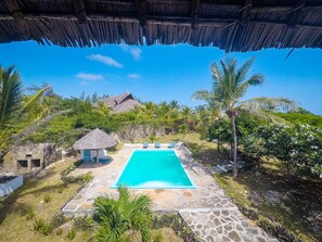 A swimming pool surrounded by stone tiles, palm trees, and a thatched-roof hut. - Ocean Breeze Villa (Watamu)