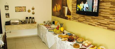 Mesa de buffet con diversos alimentos y un televisor montado en la pared.